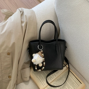 Détail du sac cabas noir avec breloque peluche blanche et sangle en perles de bois élégantes