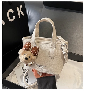 Close-up of cream white bucket bag with pebble texture and cute plush bear charm