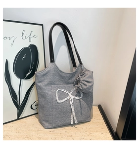 Detail of grey knitted tote bag with white lace bow and black leather handles