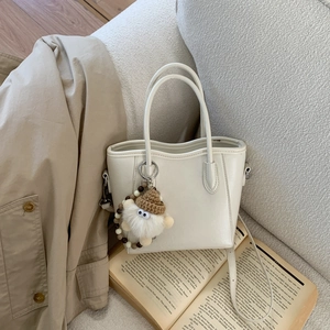 Détail du mini sac seau beige avec charme de monstre posé sur un canapé en tissu