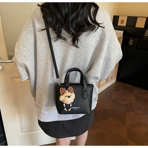 Detail view of a black pebble leather mini bag with a cute bear charm on a model's back