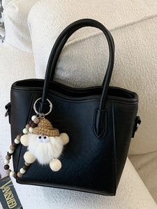 Sac à main seau noir élégant avec chaîne perlée et breloque peluche sur canapé