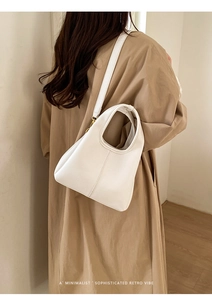 Close-up of white lychee pattern leather bucket bag with golden hardware on a trench coat