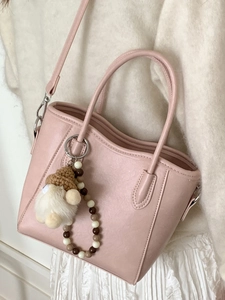 Sac seau élégant en cuir rose avec pendentif en peluche porté par un mannequin en blanc