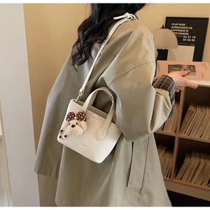 White lychee leather bucket bag featuring a teddy bear charm and brown polka dot bow detail