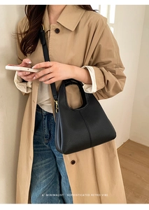 Detail of black pebbled leather bucket bag with gold hardware worn by model in trench coat