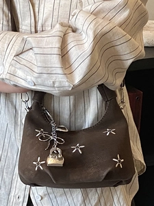 Brown matte half-moon shoulder bag with silver flower rivets and chain pendant detail