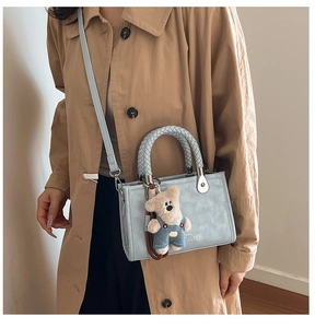 Detail view of light blue textured handbag featuring a cute plush bear charm on the strap