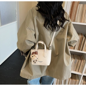 Detailed back view of off-white mini bucket bag with teddy bear charm and sleek shoulder strap