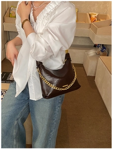 Détail d'un sac à bandoulière en cuir verni marron foncé avec une grosse chaîne dorée décorative