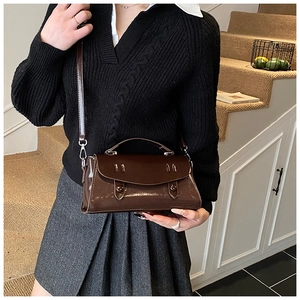 Detail of a dark brown glossy baguette bag with vintage flap worn by a model in a warm setting