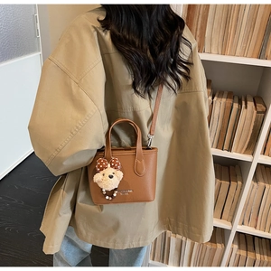 Brown lychee leather bucket bag with plush bear charm and adjustable shoulder strap