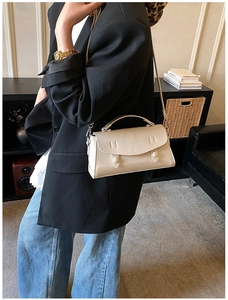 Detail of a beige leather shoulder bag with top handle and adjustable strap on a model