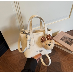 Detail of cream bucket bag with pebble texture, brand logo, and cute bear charm