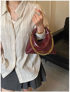 Détail d'un sac à main bordeaux en cuir verni avec une grosse chaîne dorée et fini brillant