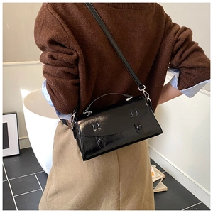 Model wearing a black glossy rectangular handbag with elegant top handle and thin strap