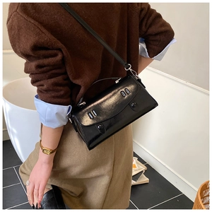 Close-up of black glossy PU leather crossbody bag featuring silver double-hole buckle detail