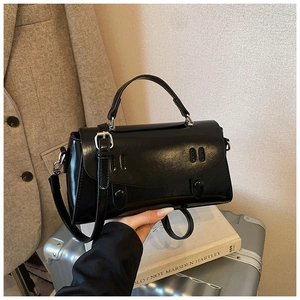 Detail of black glossy leather handbag with elegant stitching on a travel suitcase
