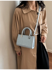 Detail of light blue crossbody bag with woven handles and fashion print text