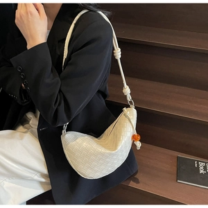 White woven leather hobo bag with knotted shoulder strap shown on a dark wooden staircase