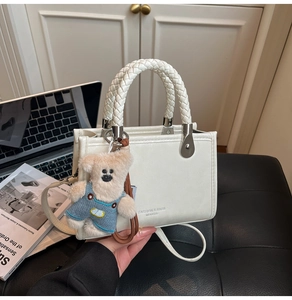 Detailed shot of white square bag with braided handle and cute teddy bear charm