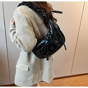 Close-up of black glossy patent leather shoulder bag with pleated strap and knot detail