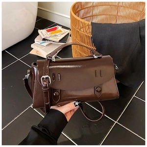Detailed close-up of dark brown glossy patent leather crossbody bag with silver hardware