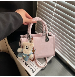 Pink PU leather handbag detail with woven handle and plush bear charm on books