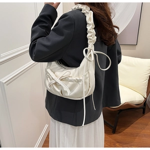 Close-up of cream white dumpling bag with ruffles and cute bow accents on PU leather