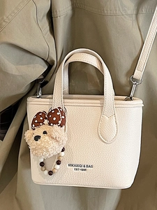 Minimalist cream textured leather bucket bag with bear charm and beaded strap