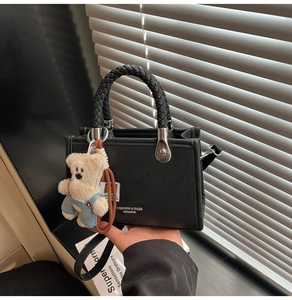 Detail of black PU leather square bag with woven ring handle and plush bear charm accessory