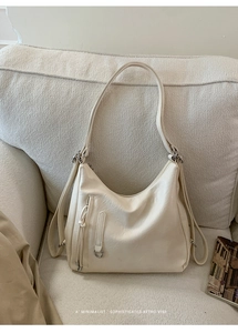 Detail view of a cream beige minimalist hobo bag showing faux leather texture on a sofa