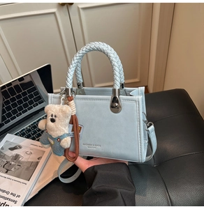 Detail of light blue square handbag featuring white woven handle and cute bear charm