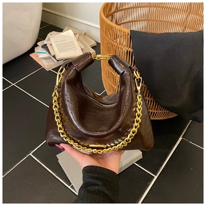 Gros plan sur un sac en cuir verni marron foncé avec une grosse chaîne en métal doré chic