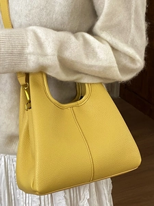 Yellow pebbled leather bucket bag with top handle and shoulder strap worn by a model