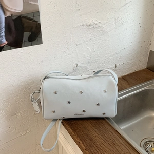 Detail of white cylinder bag featuring silver star rivets and embossed brand logo