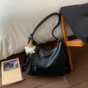 Detail of black faux leather Hobo bag with adjustable strap and cream knit charm on sofa