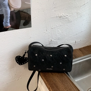 Close-up of black leather crossbody bag featuring silver star rivets and heart charm
