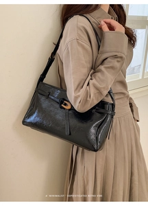 Chic black glossy shoulder bag with a gold buckle shown on a model in a retro style
