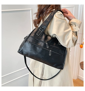 Detail of a large black leather tote bag with three zipper pockets on a model in a trench coat
