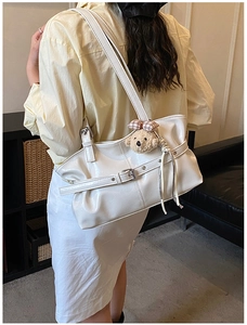 Détail d'un sac sous les bras blanc avec un charmant pendentif d'ours en peluche marron