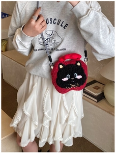 Close-up of cute plush red apple bag with a black cat face and woven shoulder strap