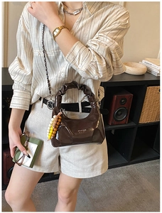 Detailed close-up of dark brown glossy handbag featuring pleated handles and beaded charm