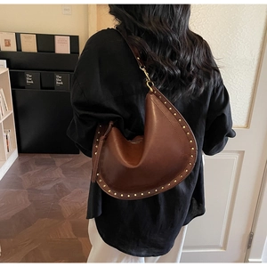 Detailed back view of a caramel leather crescent bag with golden studs on a female model