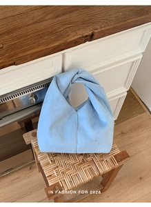 Detail of light blue suede mini handbag with minimalist twist handle on wooden stool