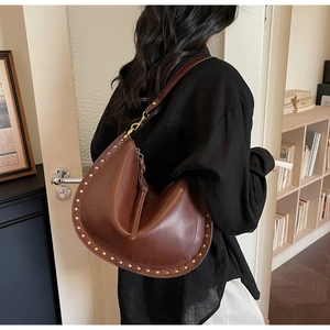 Side view of dark brown leather hobo bag with gold rivet detailing on a female model