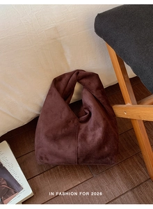 Detail of a dark brown suede handbag with a unique twisted handle in a minimalist style