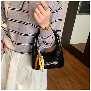 Close-up of black patent leather crescent bag with pleated handle and beaded charm detail