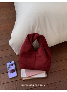 Detail view of burgundy suede pleated cloud bag resting on books in a cozy setting
