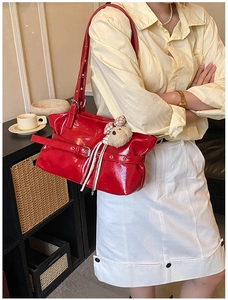 Détail du sac bandoulière en cuir verni rouge avec boucles et accessoire ourson